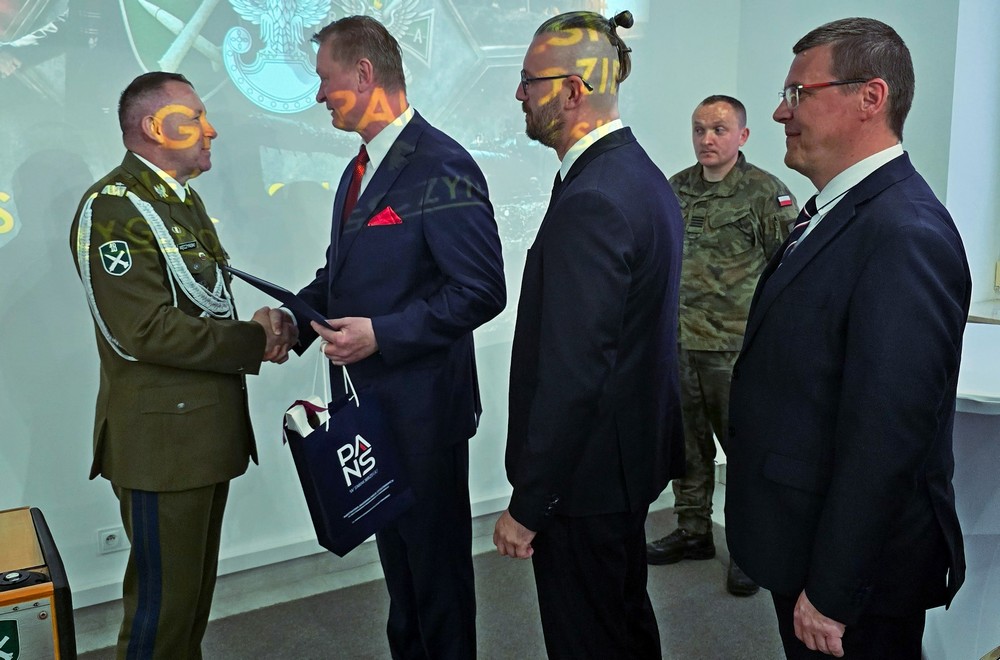 Na zdjęciu z lewej, Rektor PANS dr hab. Paweł Maciaszczyk, Kanclerz PANS mgr Piotr Bordun oraz wykładowca PANS dr hab. Krzysztof Chochowski, składają gratulacje płk. Piotrowi Męczyńskiemu z okazji nadania mu stopnia generała brygady  